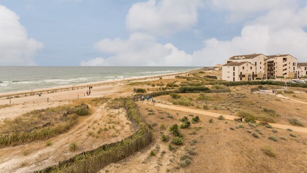Une zone côtière dotée d’une plage de sable, d’un sentier pédestre et d’un ensemble d’immeubles à plusieurs étages, avec des balcons donnant sur la plage.