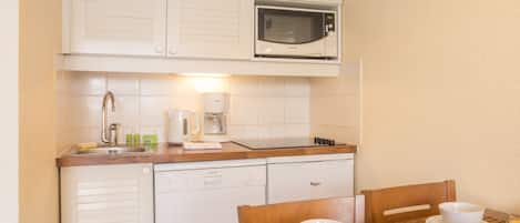 A compact kitchen with a microwave, coffee maker, and dishwasher. There is a breakfast table with croissants, juice, and a bowl.