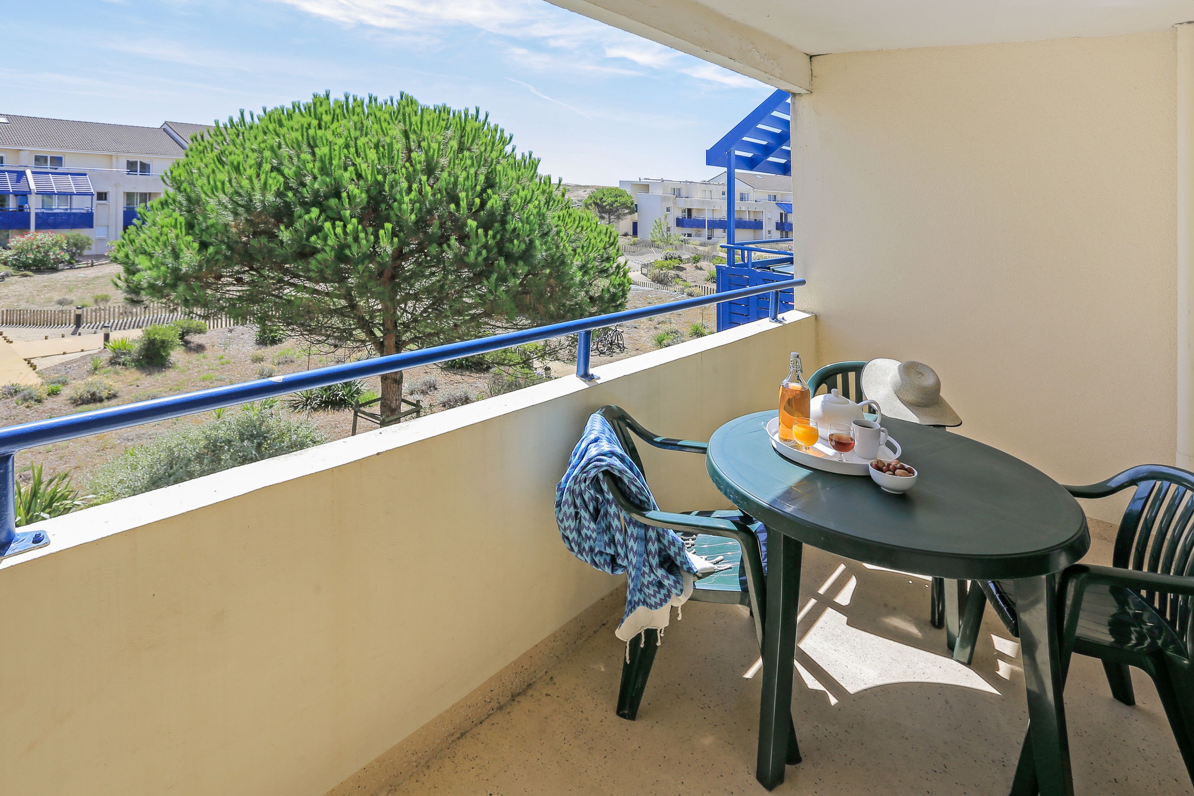 Un balcon avec une table et des chaises, une vue sur un arbre et des immeubles, et une balustrade.