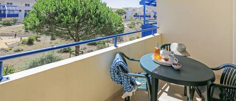 Un balcon avec une table et des chaises, une vue sur un arbre et des immeubles, et une balustrade.