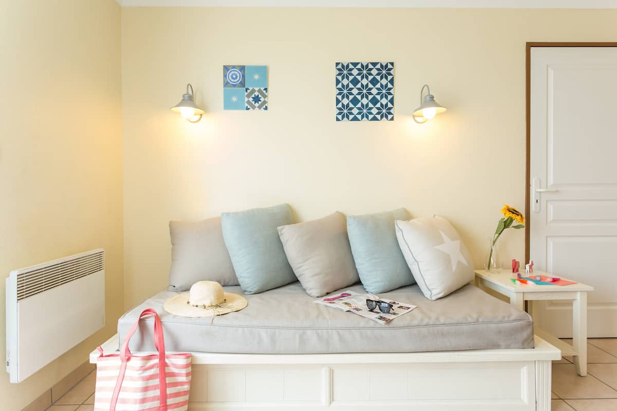 Une chambre à coucher avec un lit, des oreillers, une table de chevet ornée d’un vase et d’une fleur, un sac à rayures et un chapeau.