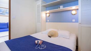 A neatly made bed with a blue blanket, a beige hat, and a pair of headphones on it.
