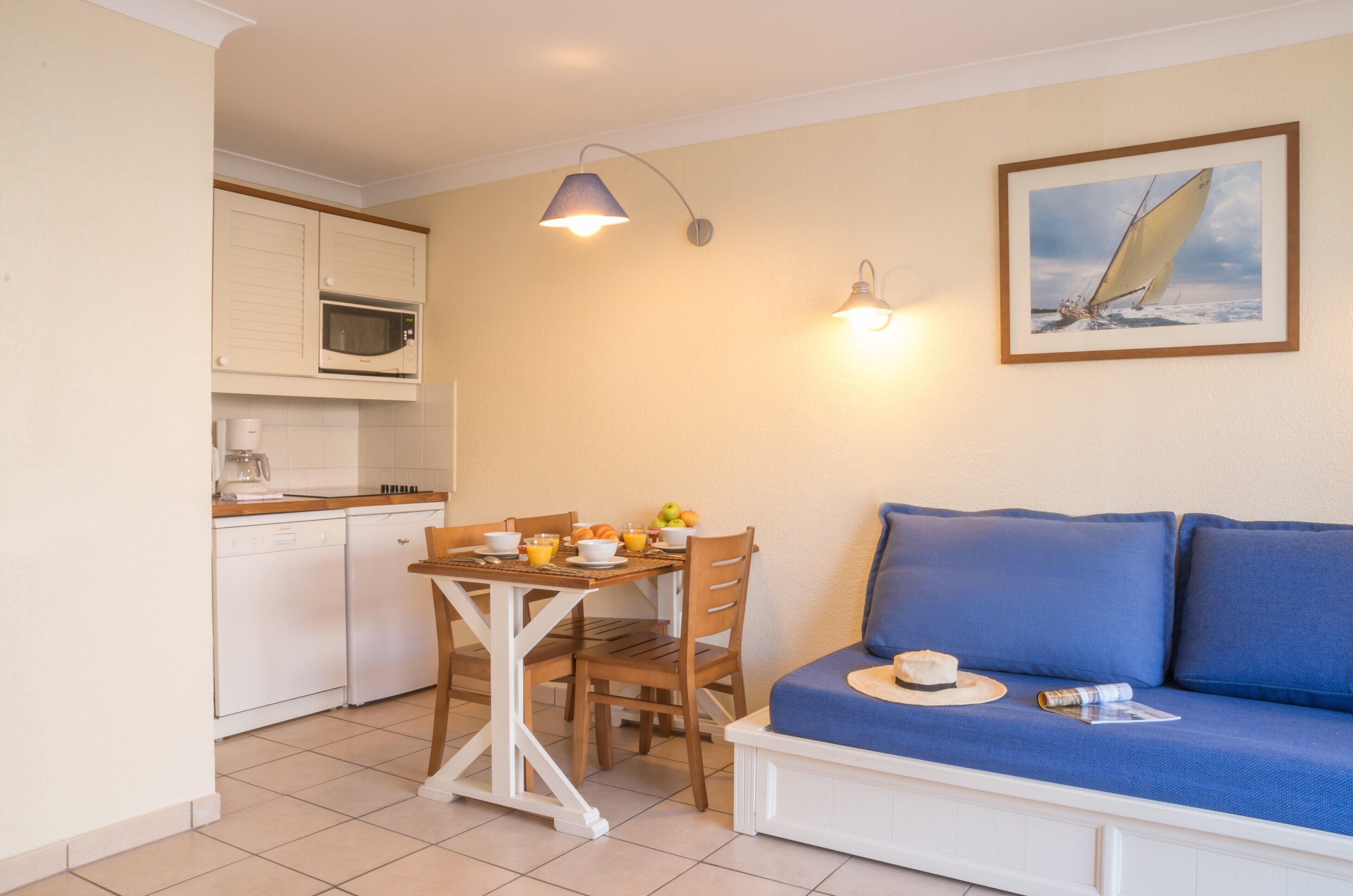 A compact kitchen with a dining table, chairs, and a blue sofa.