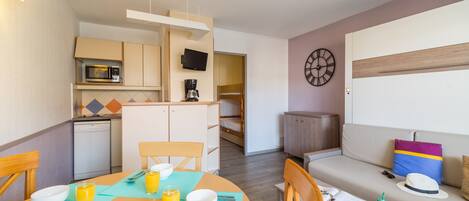 A compact living space with a kitchenette, dining area, and a sofa with a colorful cushion.