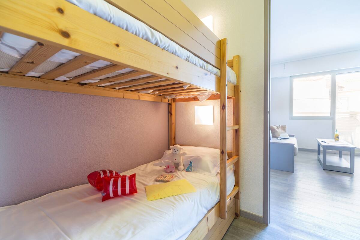 Una cama nido con escalera de madera, una mesita de noche pequeña y una ventana.