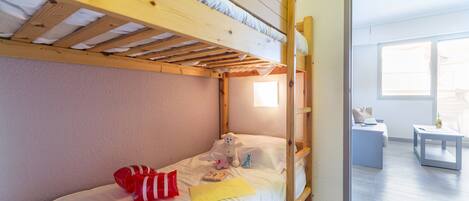 A bunk bed with a wooden ladder, a small bedside table, and a window.