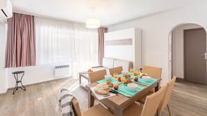 Uma área de refeições moderna com uma mesa de madeira, cadeiras de vime e uma mesa de café da manhã com croissants, maçãs e suco de laranja.