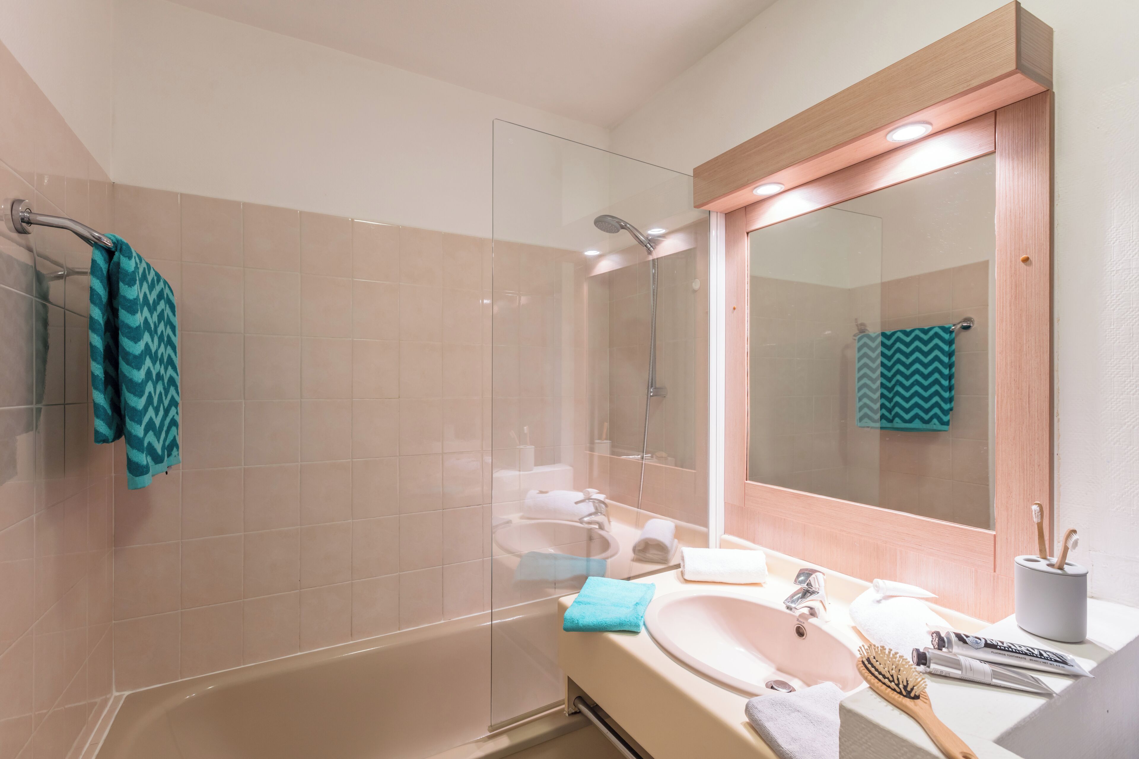Un baño con ducha de vidrio, lavamanos con espejo y un perchero para toallas.