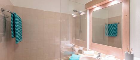 Un baño con ducha de vidrio, lavamanos con espejo y un perchero para toallas.