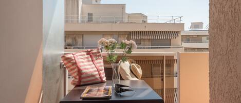 A balcony with a table set with a magazine, a vase with flowers, and a striped pillow.
