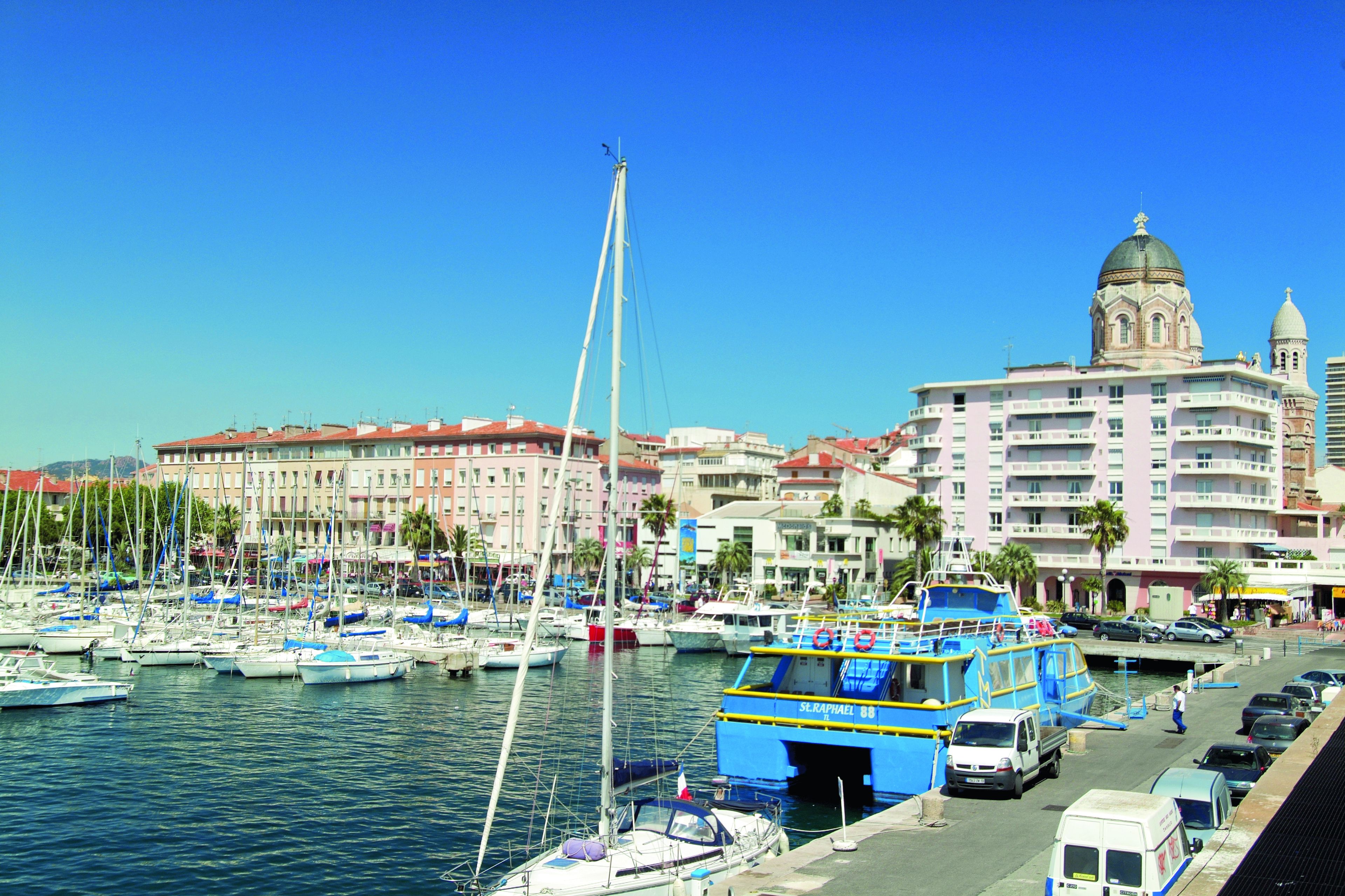 A marina with boats, a blue and yellow boat, and a building with a dome and tower.