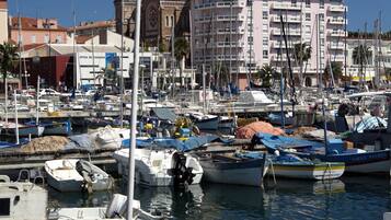 A marina with various boats docked, a prominent building with domed architecture in the background, and a clear blue sky.