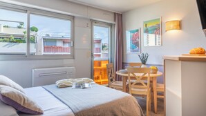 Une chambre d’hôtel avec un lit, une petite table avec des chaises, une fenêtre donnant sur des immeubles et une lampe fixée au mur.
