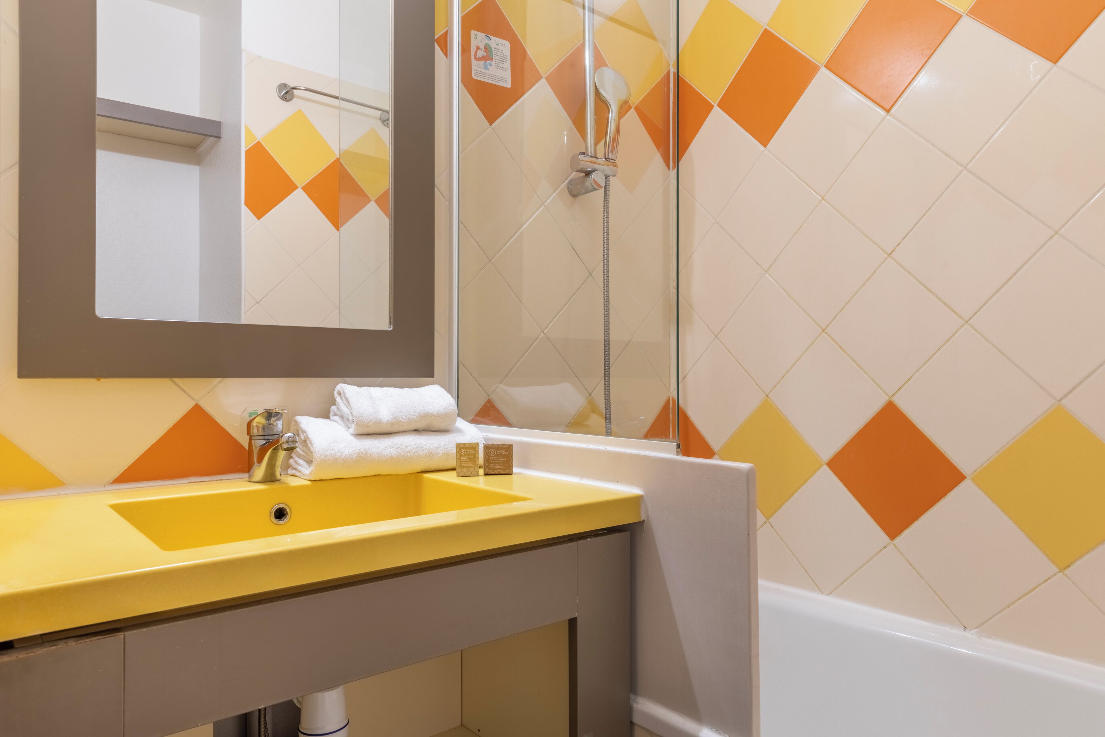 Un baño con lavamanos amarillo, un espejo y zona de ducha.