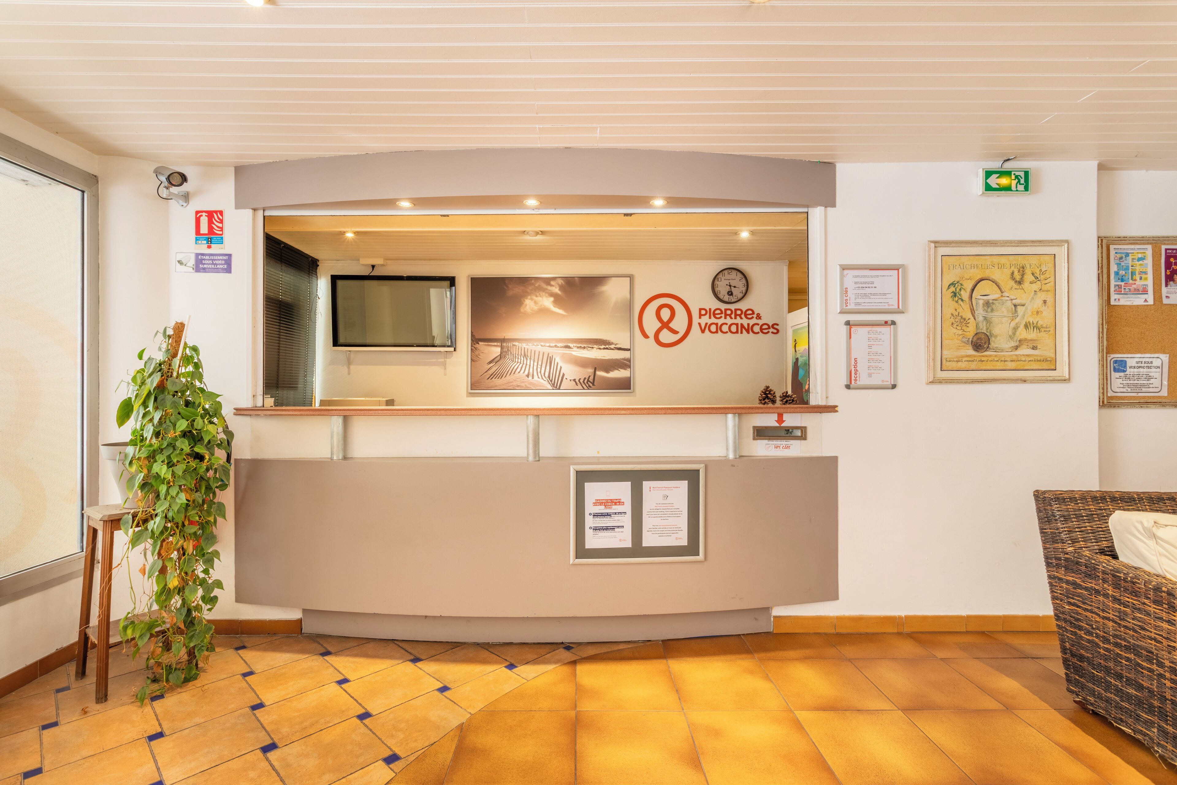 Eine Rezeption mit einem Schild, das 'Pierre & Vacances' zeigt, einer Uhr, gerahmten Zertifikaten und einem Blumentopf.