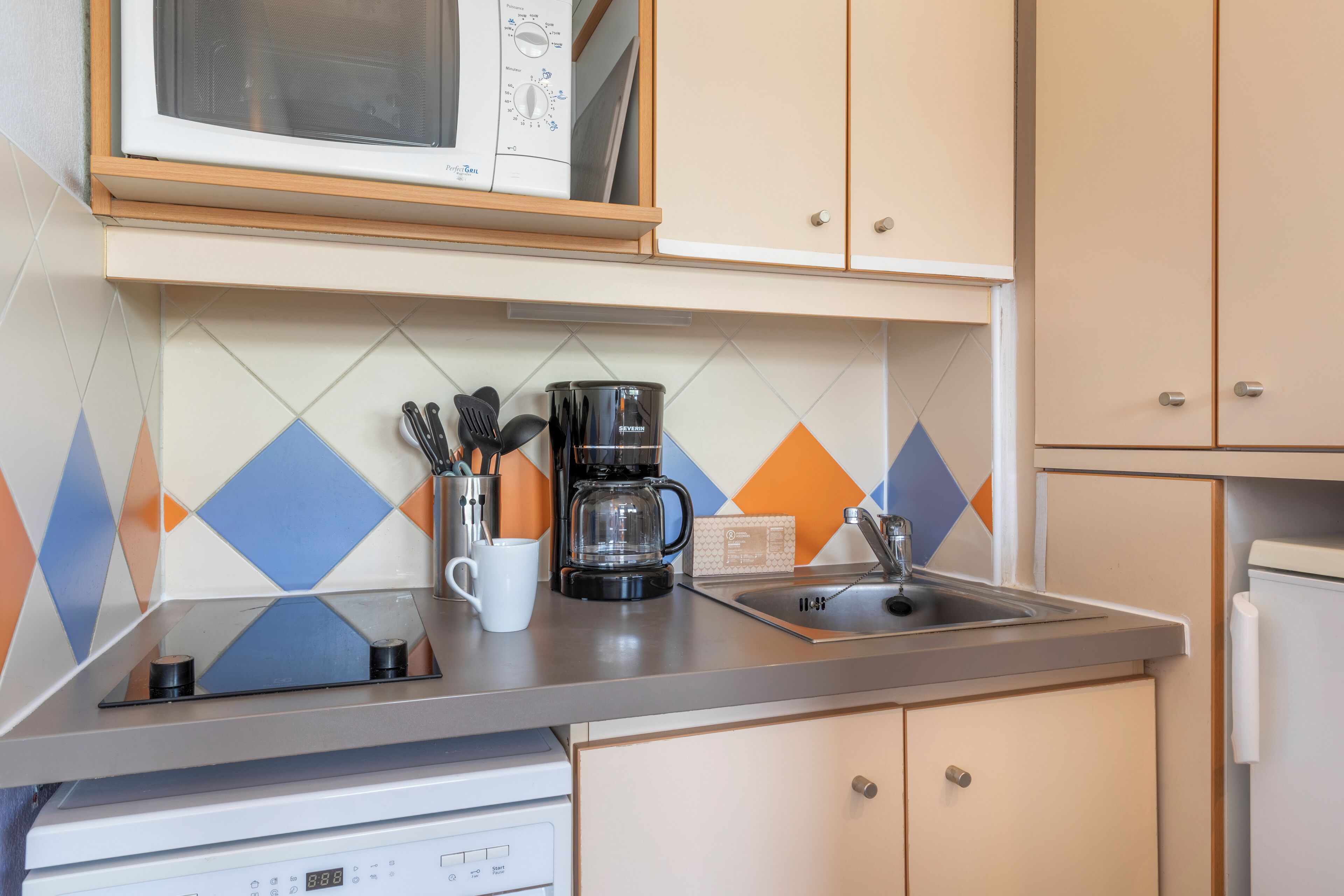 Une cuisine équipée d’un four à micro-ondes, d’une machine à café et d’ustensiles de cuisine, le tout posé sur le plan de travail.