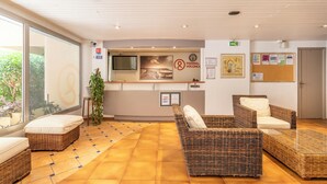 Un espace d’accueil avec des meubles en osier, un téléviseur et un tableau d’affichage.
