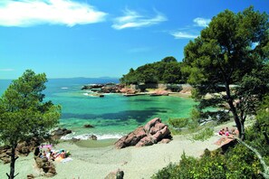 A beach with clear turquoise water, rocky outcrops, and dense green trees. - Pierre & Vacances Résidence Promenade des Bains (Saint-Raphael)