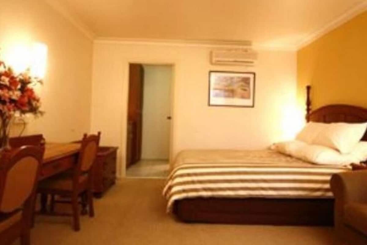 Ein Hotelzimmer mit einem Bett, einem Schreibtisch und Stühlen. Eine Tür führt in einen weiteren Raum.