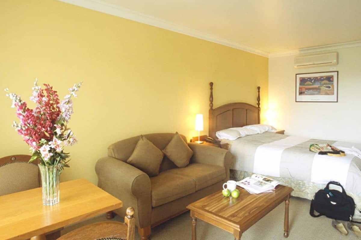 Ein Hotelzimmer mit einem Bett, einem Nachttisch aus Holz, einem Holztisch, einer Couch und einem Blumenstrauß.