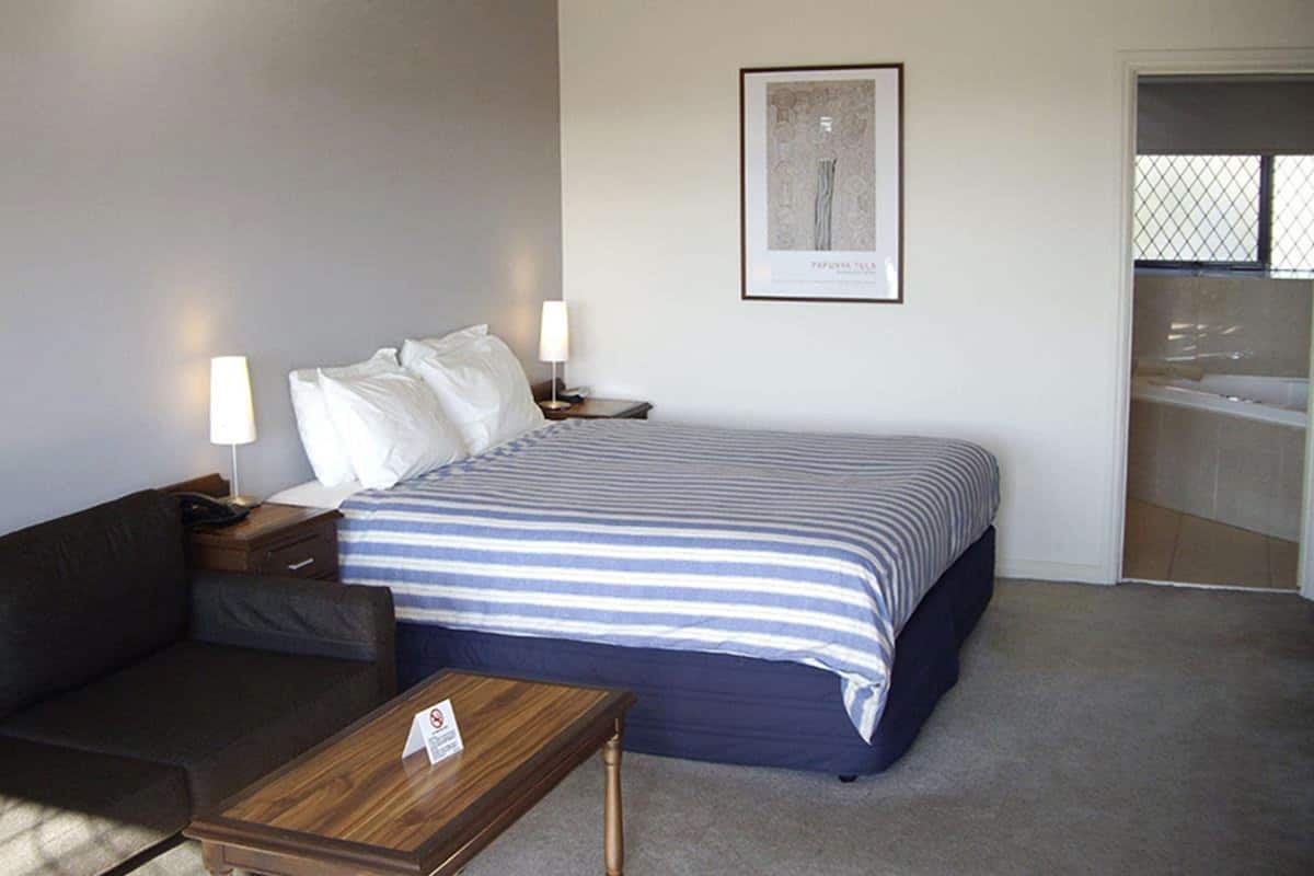 Ein Hotelzimmer mit Bett, Sofa, Nachttisch, Lampe und einem gerahmten Bild an der Wand.