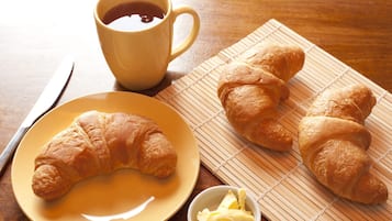 A wooden table with a yellow plate, a yellow cup, and two croissants.