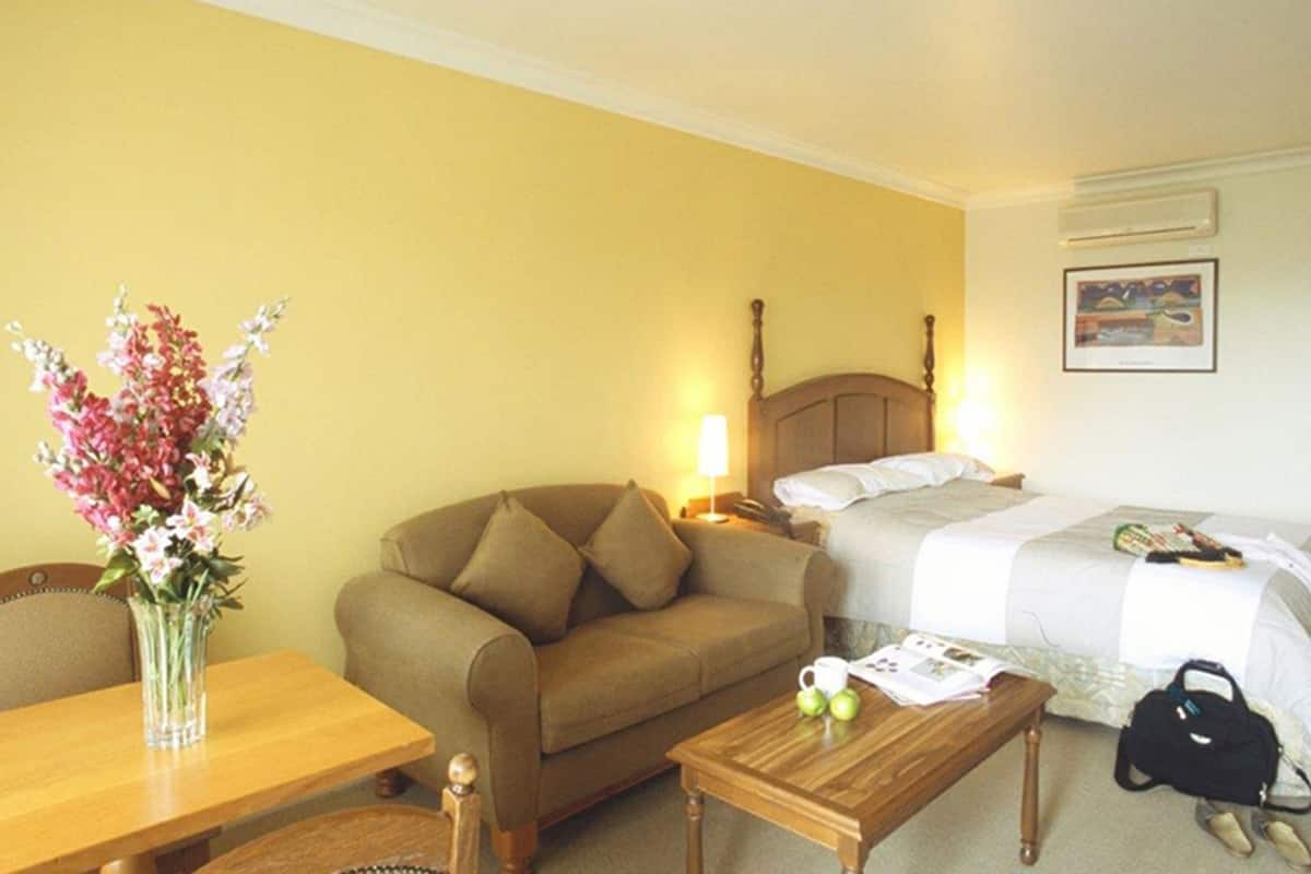 Ein Hotelzimmer mit Bett, Sofa, Couchtisch aus Holz, einem kleinen Tisch mit Blumenvase und einer Wand-Klimaanlage.