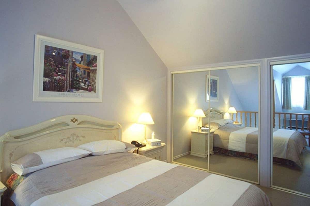 Ein Schlafzimmer mit einem Bett, Nachttischlampen, einem Nachttisch, einem Spiegel und einem gerahmten Bild an der Wand.