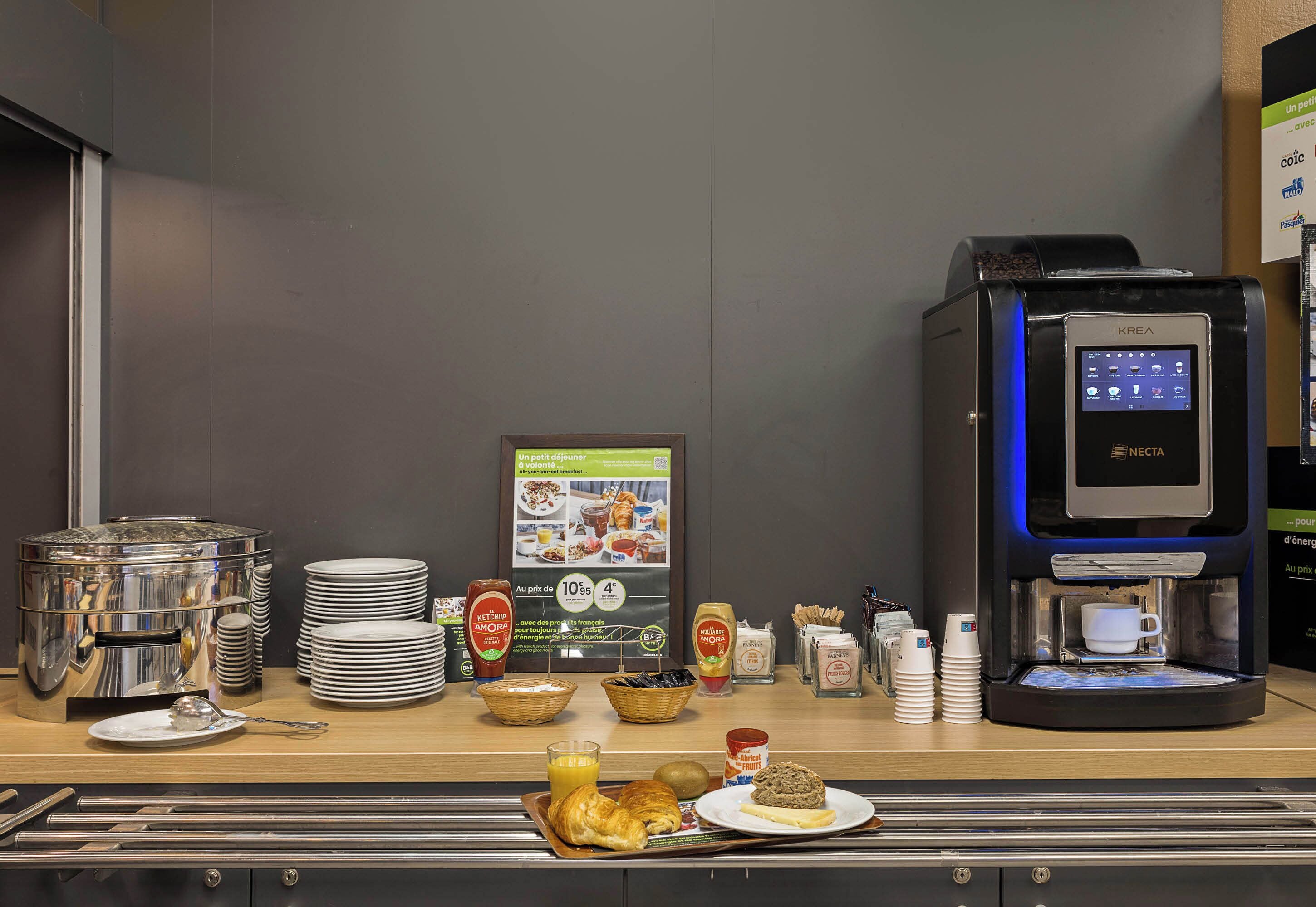 Un buffet de petit-déjeuner comprenant une machine à café, des assiettes, des condiments et divers aliments.