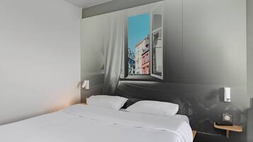 A modern hotel room with a large bed, a nightstand with a remote control, and a wall mural of a cityscape.