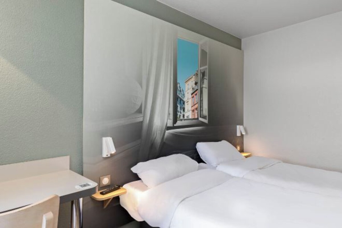A hotel room with a bed, bedside tables, and a wall mural of a cityscape.