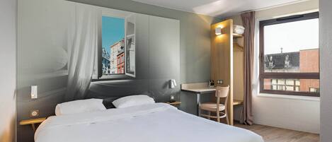 A hotel room with a large bed, a desk, a chair, a window with a view of buildings, and a wall with a cityscape mural.