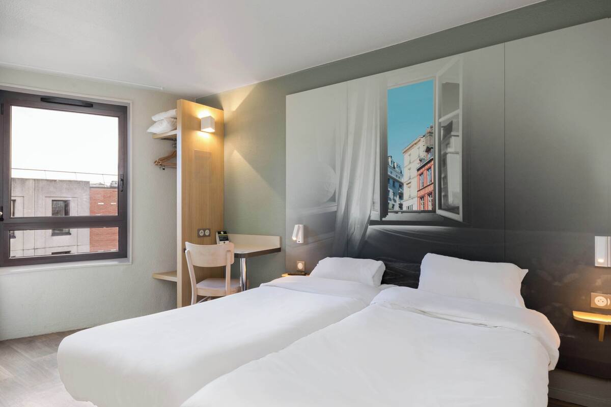 Quarto de hotel com duas camas, uma escrivaninha e uma cadeira.