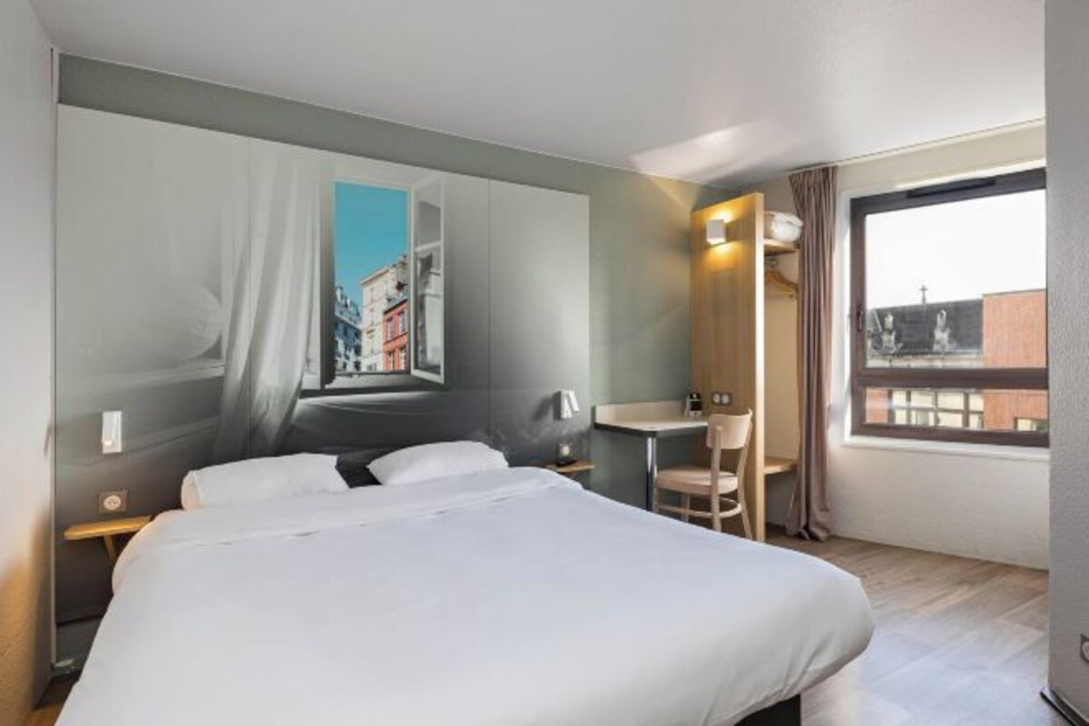 A hotel room with a bed, a desk, a chair, and a large window.