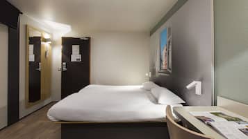 Une chambre d’hôtel avec un lit, un bureau et une chaise. On y trouve des portes et une fenêtre donnant sur des immeubles.