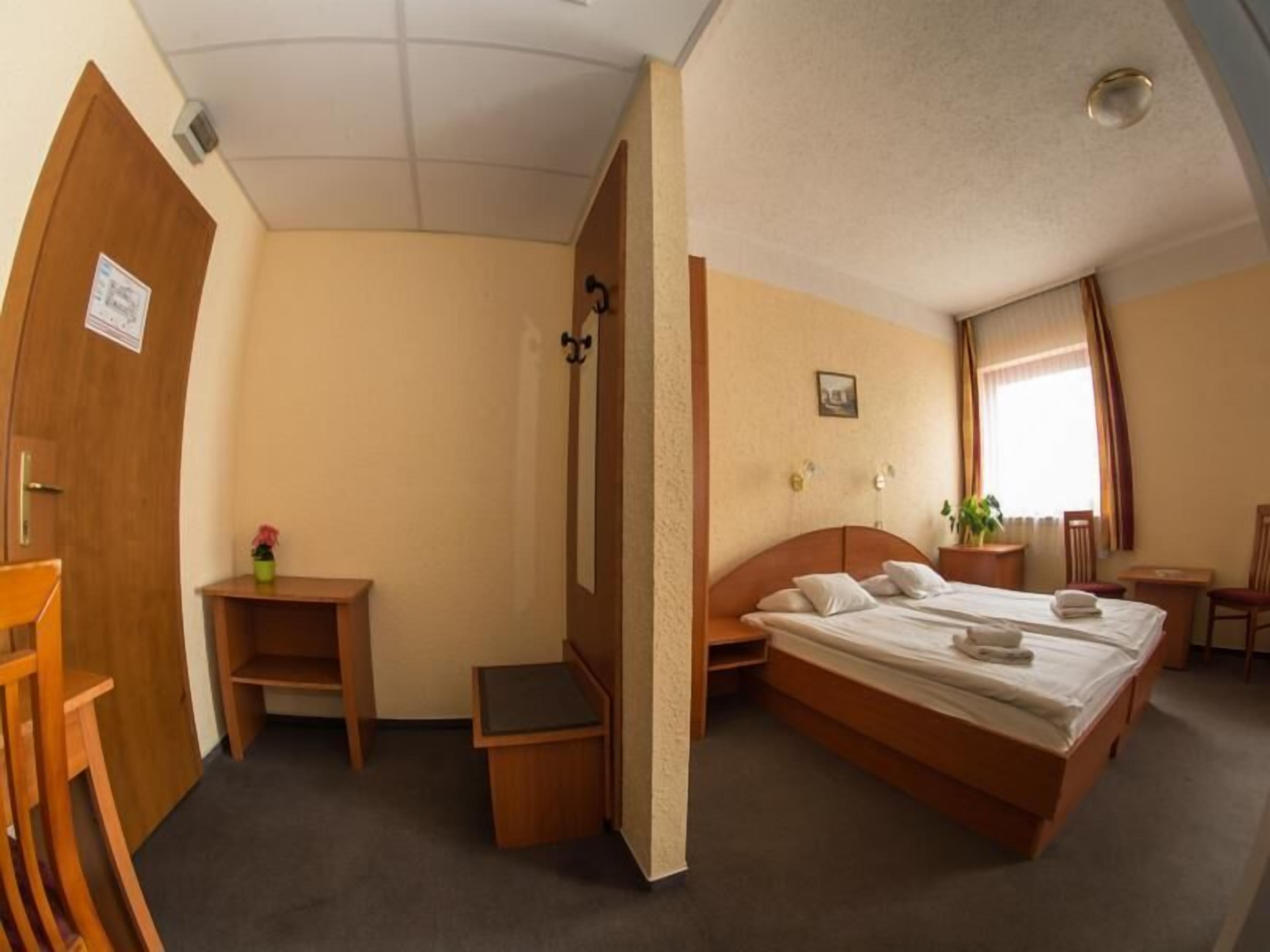 A hotel room with a single bed, a small desk, a chair, a nightstand, and a window with curtains.