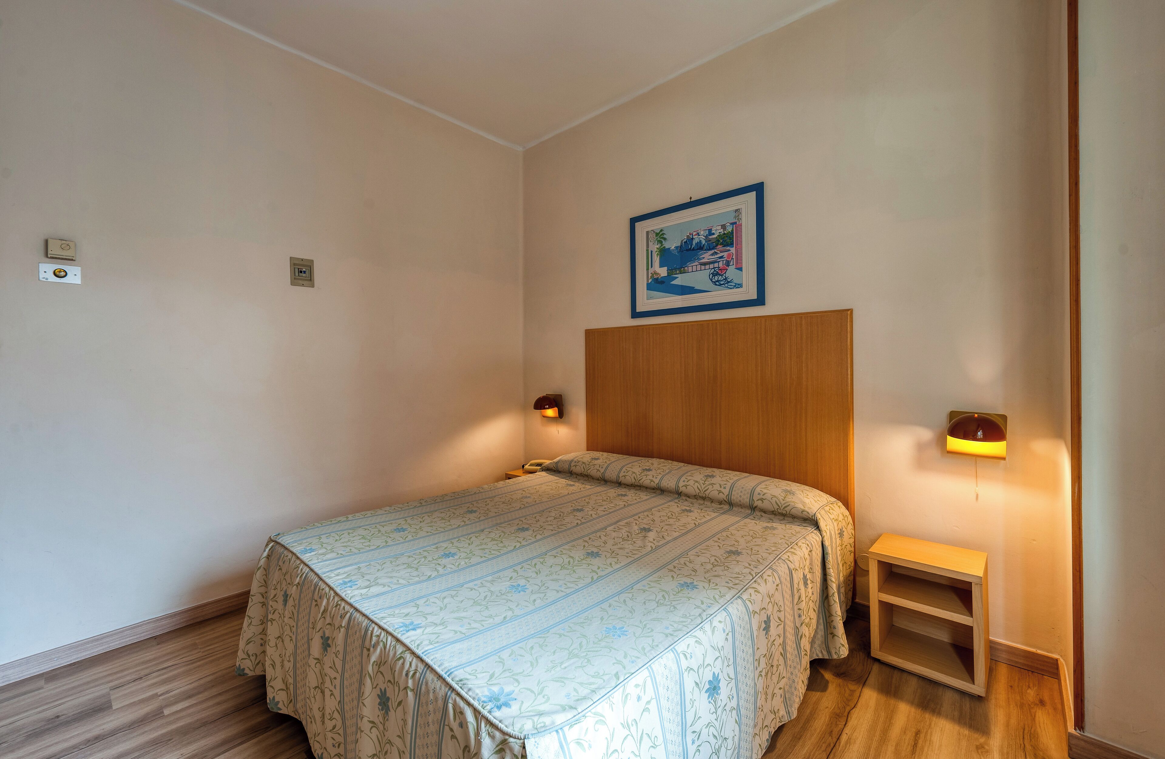 Un dormitorio con una cama, lámparas de noche, una mesita de noche y un cuadro en la pared.