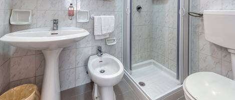 Un baño con lavamanos pedestal, bidé, inodoro y ducha con mampara de vidrio.