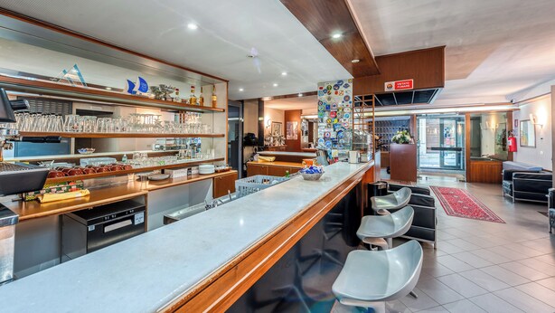 A modern bar area with a long counter, seating, and a variety of glassware and bottles. - Barsotti Hotel (Brindisi)