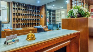 A hotel reception desk with a wooden panel backdrop, a bell, and a sign indicating the hotel name. - Barsotti Hotel (Brindisi)