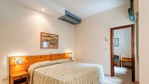 A bedroom with a bed, bedside tables, a wall-mounted air conditioner, a framed picture, and a wooden door leading to another room. - Barsotti Hotel (Brindisi)