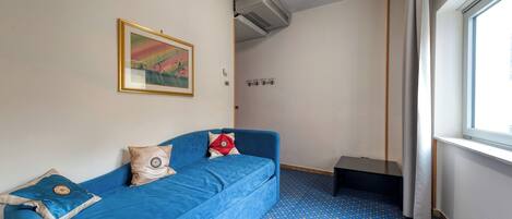 A room with a blue sofa, a framed picture on the wall, and a window with curtains.