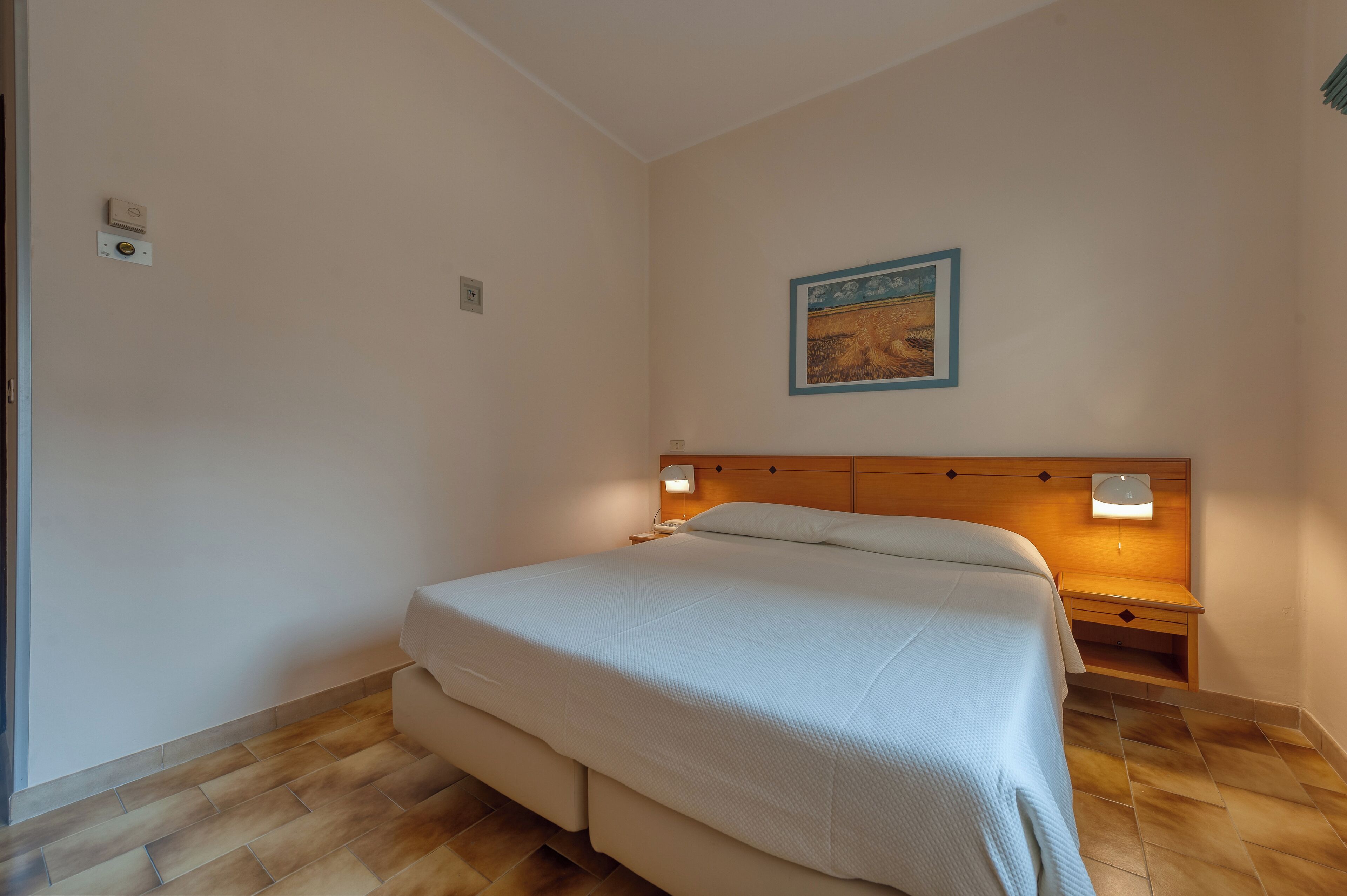 Un dormitorio con cama, mesitas de noche, lámpara de pared y un cuadro enmarcado.