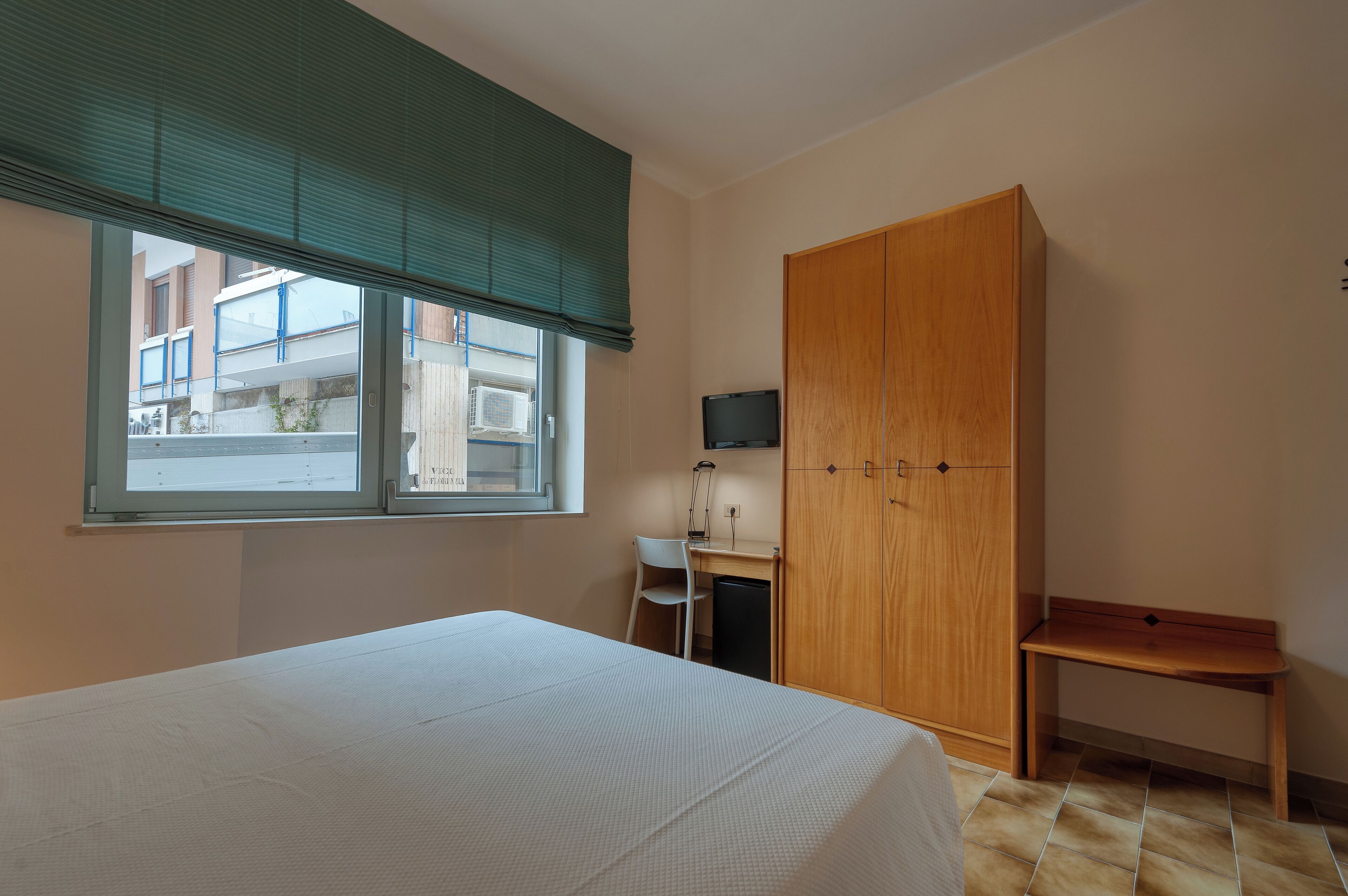 Un dormitorio con cama, escritorio, silla, armario y televisor.