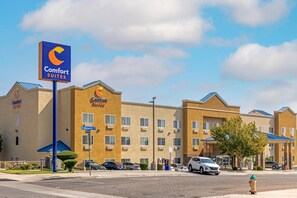 Un hotel Comfort Suites con un letrero azul llamativo, edificios de varios pisos y un estacionamiento con varios automóviles.