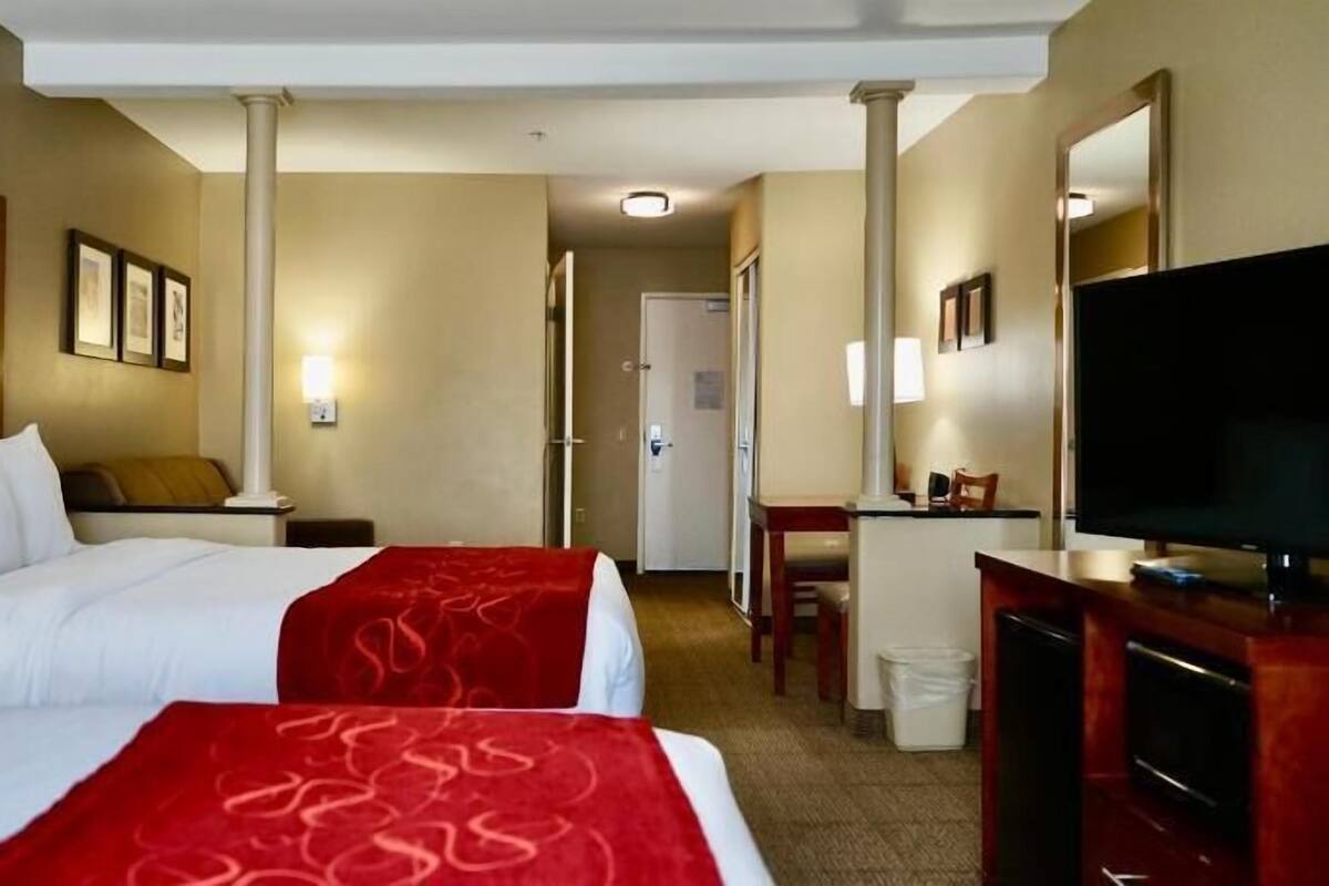 A hotel room with two beds, a desk, a television, and a mirror.