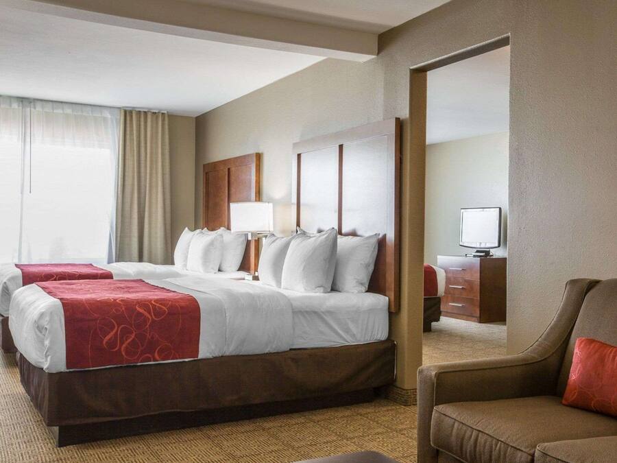 Habitación de hotel con una cama grande, dos mesitas de noche, un televisor y una zona de estar con una silla y reposapiés.