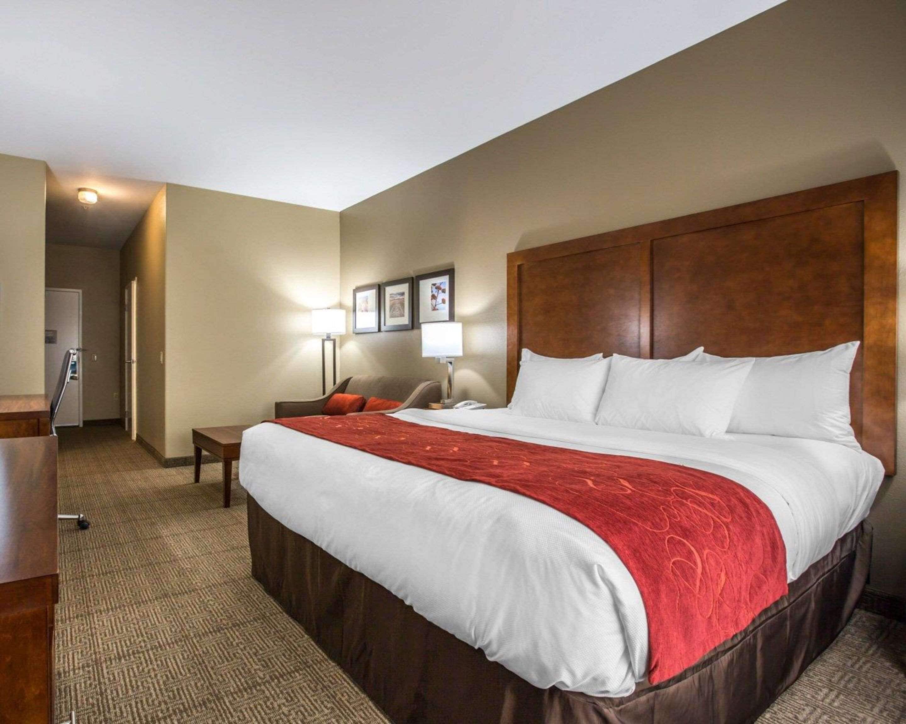 A hotel room with a large bed, a desk, a chair, a nightstand, and a lamp.