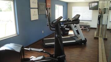 A fitness center with treadmills and elliptical machines, motivational posters on the wall, and a large mirror.