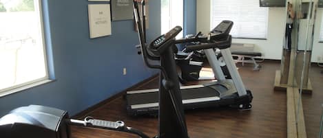 A fitness center with treadmills and elliptical machines, motivational posters on the wall, and a large mirror.